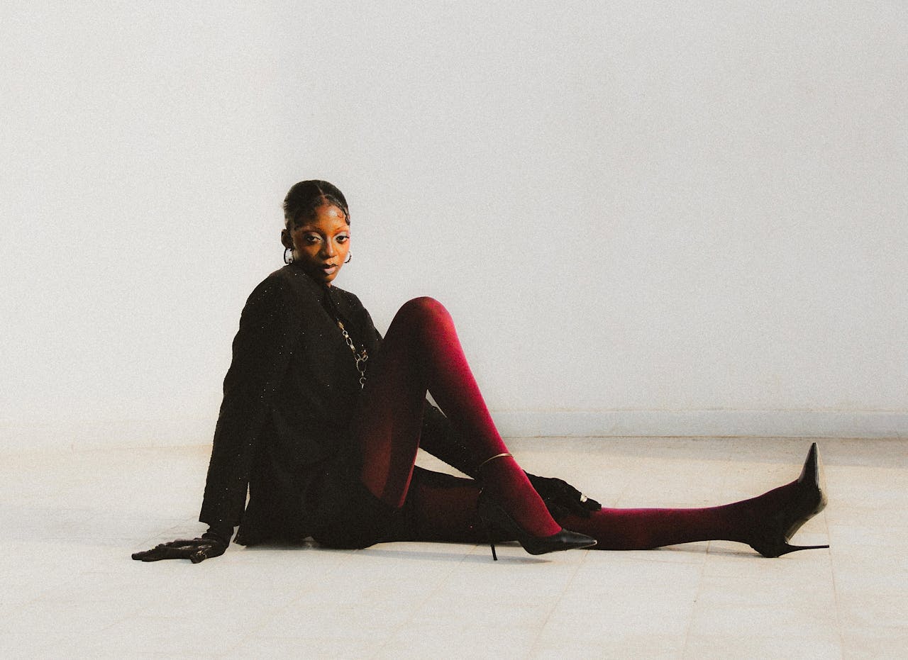 gallery-05 Stylish woman in red tights sitting against a minimalist white background.